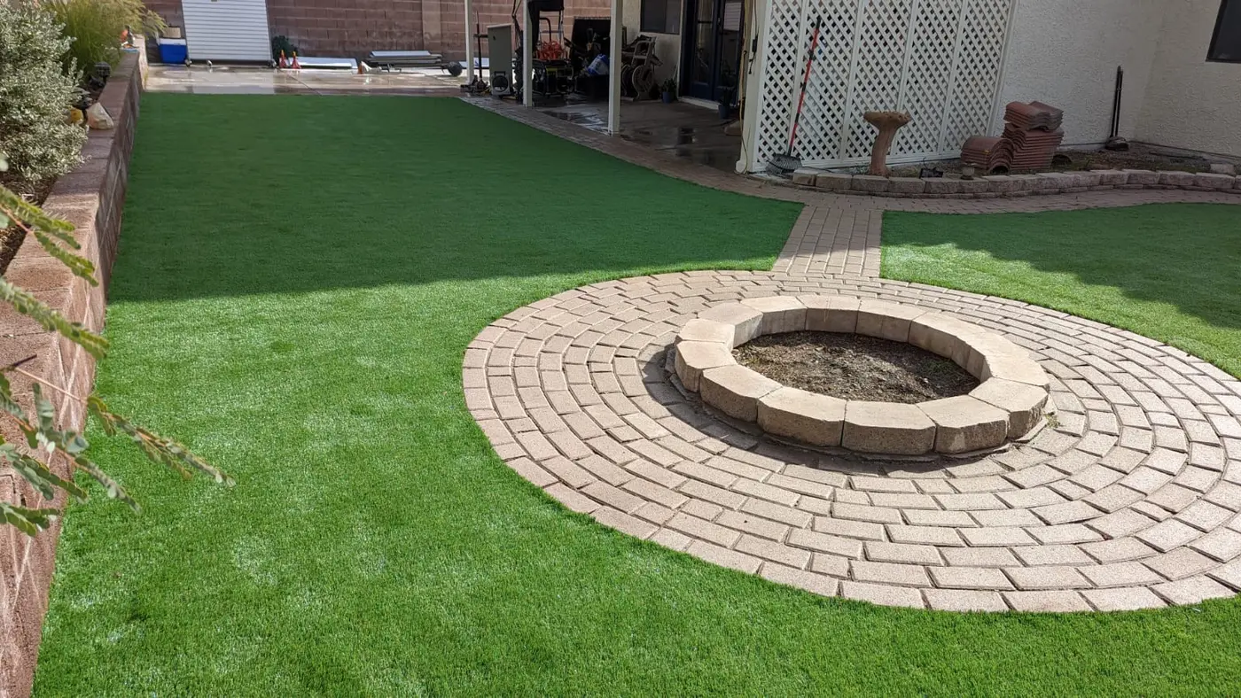 Round paver fire pit surrounded by artificial turf